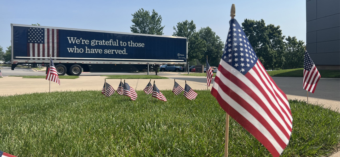 Flags in grass and Tyson truck with text "We're grateful to those who have served.